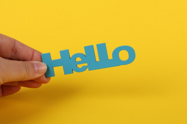 Fotografia de uma pessoa a segurar "Hello" sobre fundo amarelo