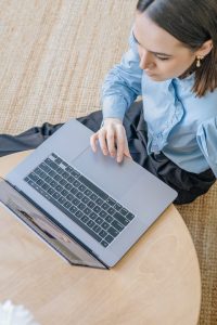 Een vrouw in blauwe lange mouwen zittend op de grond terwijl ze haar laptop gebruikt