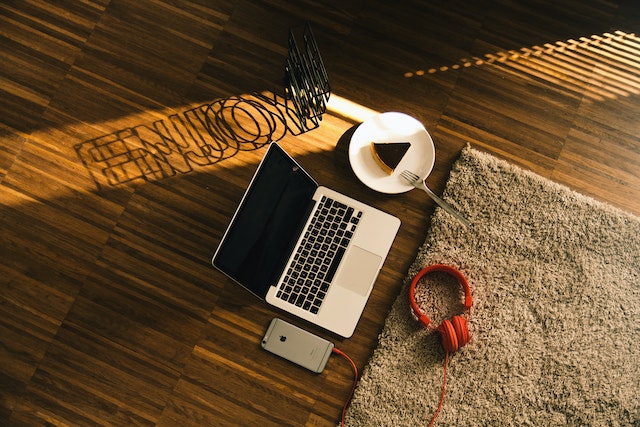 Macbook Beside Slice on Cake on Plate, Iphone and Headphones