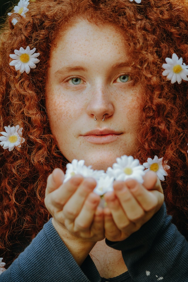 Woman with red hair and freckles holds white flowers.
