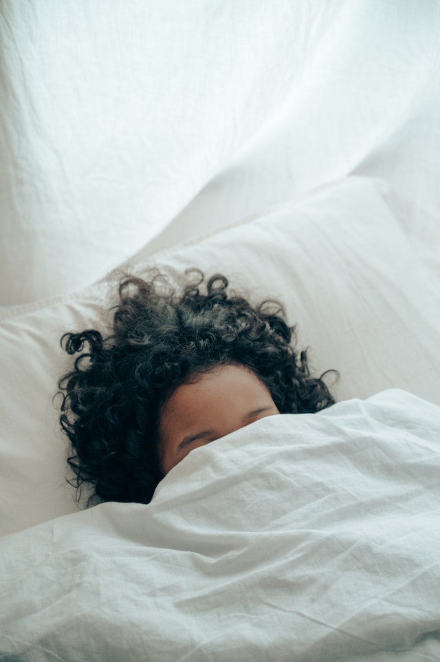 Woman with curly hair 
asleep under a blanket.
