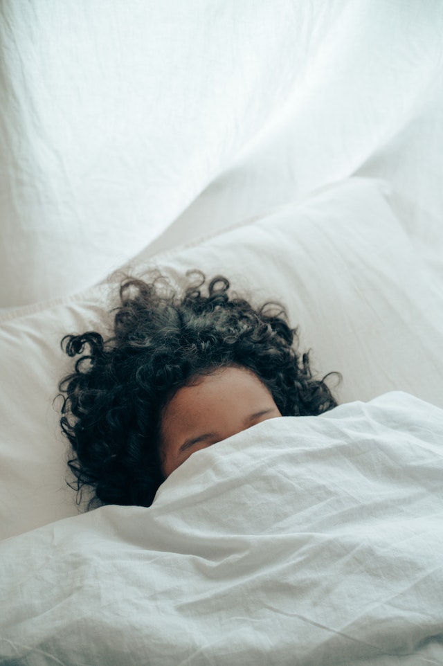 Mulher de cabelo encaracolado a dormir debaixo de um cobertor.