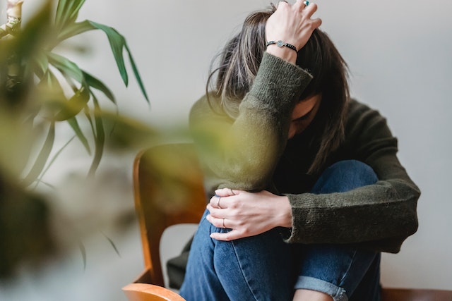 Mujer con la cabeza en la mano, agachada en una silla.