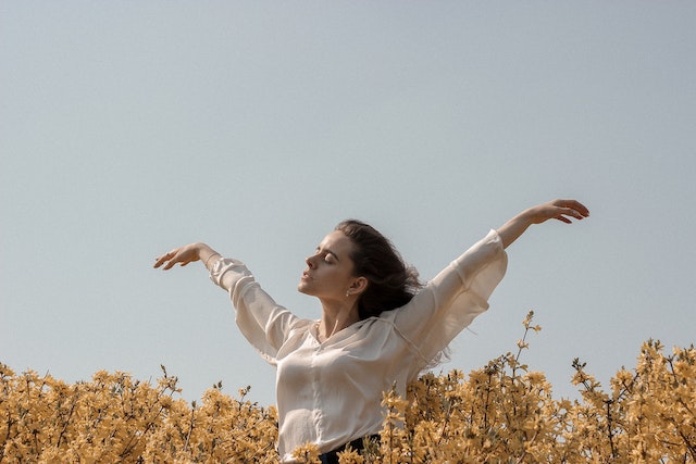 Eine Frau mit erhobenen Armen in einem Blumenfeld.