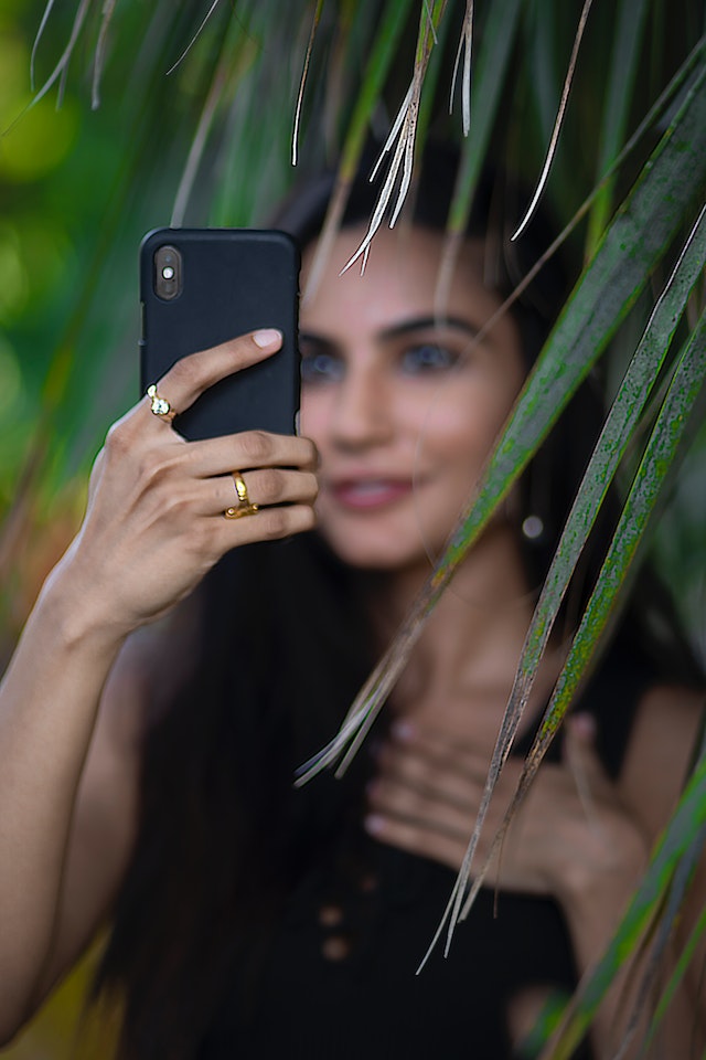 Woman taking a photo from behind the bushes.
