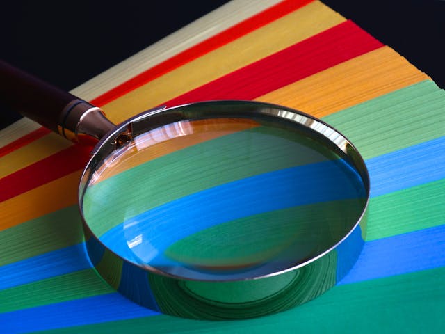 Magnifying glass with a brown handle on top of colored paper.