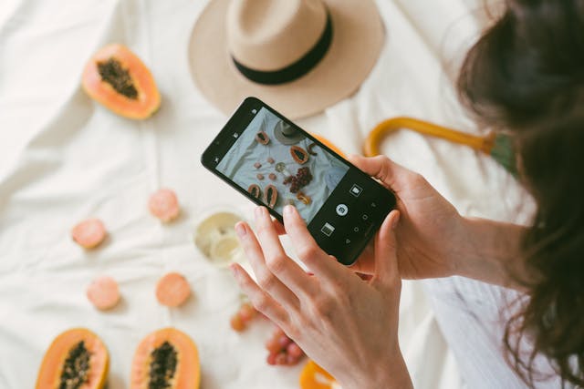 Person taking a photograph of several fruits with a black smartphone.