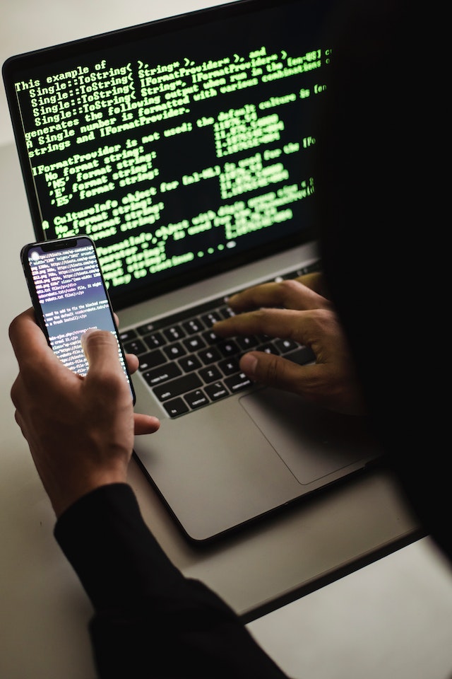 Anonieme hacker codeert op een telefoon en laptop.