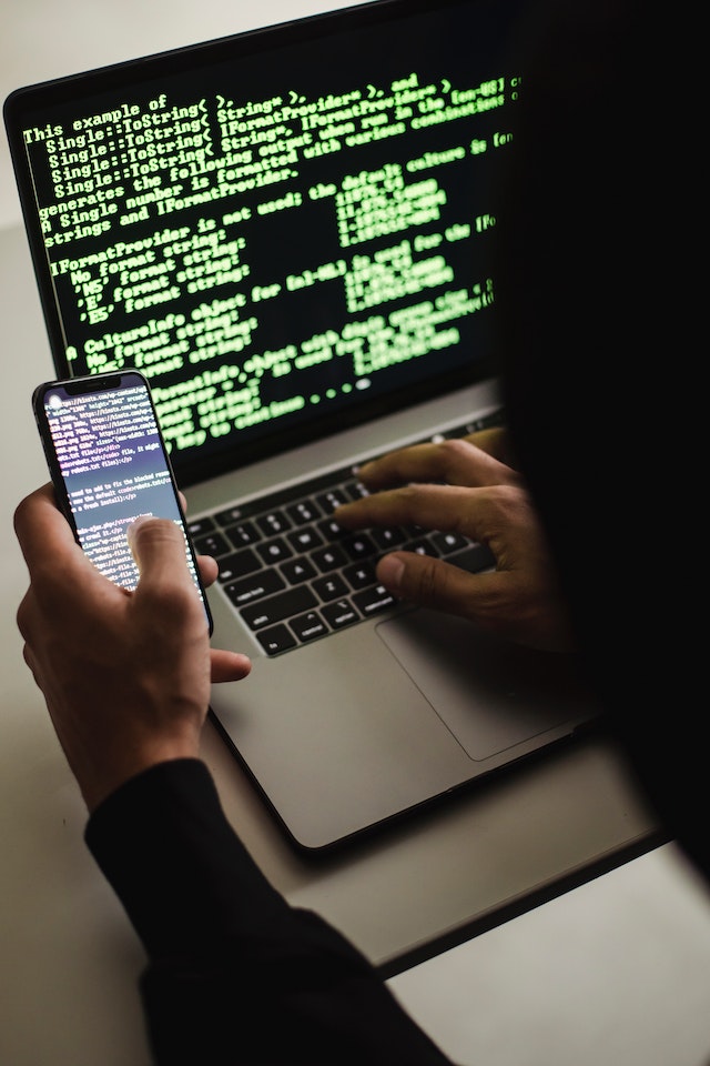 Anonymous hacker coding on a phone and laptop.