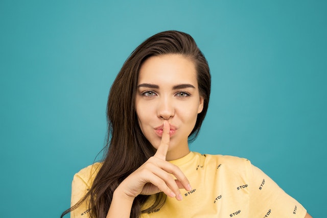 Frau mit senkrecht über die Lippen geführtem Zeigefinger.