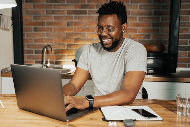 pexels-tima-miroshnichenko-5198239 | Path Social Homem a escrever no seu computador portátil com um bloco de notas e um telemóvel ao lado.