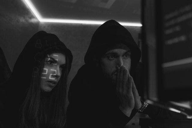 Man and woman in hoodies stare at computer screens.