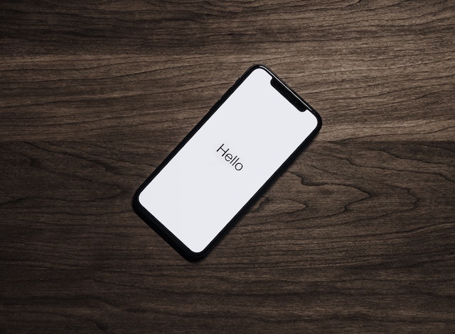 茶色のテーブルの上に置かれた黒いiPhone、画面には「Hello」の文字。