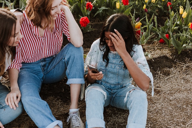 Drie vrouwen kijken naar een mobiele telefoon en bekijken door gebruikers gegenereerde inhoud om te delen.