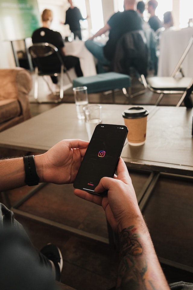 Personne non vue assise à une table avec des gens, ouvrant Instagram sur son téléphone.