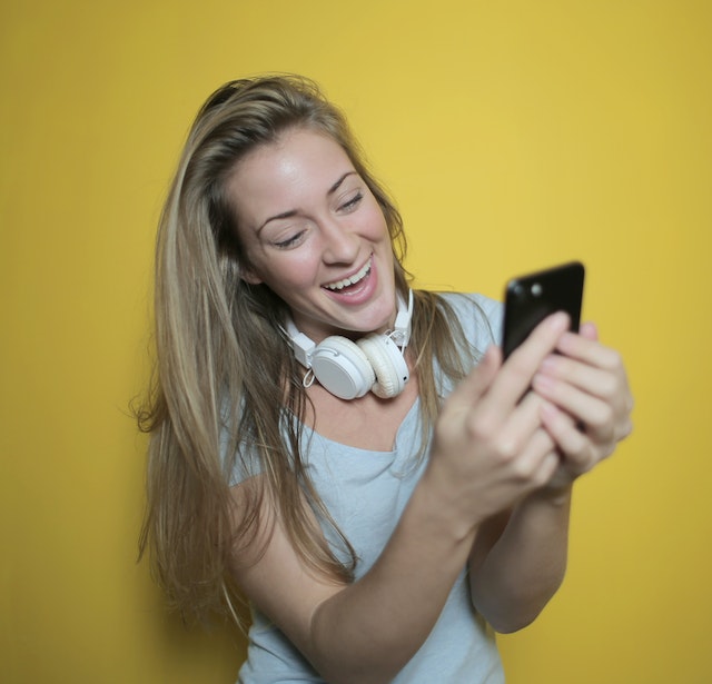 Lachende vrouw met een koptelefoon om haar nek die een foto maakt met haar smartphone.