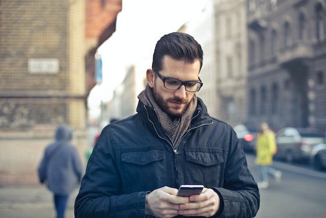 Man looking at phone in hand while on a city street.