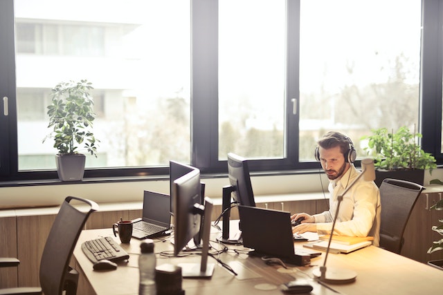 Un bărbat purtând căști în fața unui monitor de calculator într-un birou.