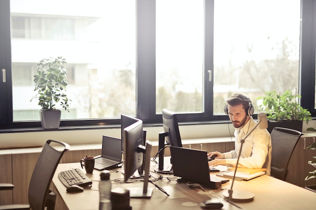 Um homem com auscultadores virado para um monitor de computador num escritório.