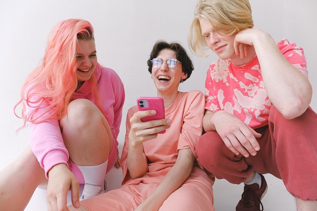  Friends in pink clothes laughing while looking at a smartphone.