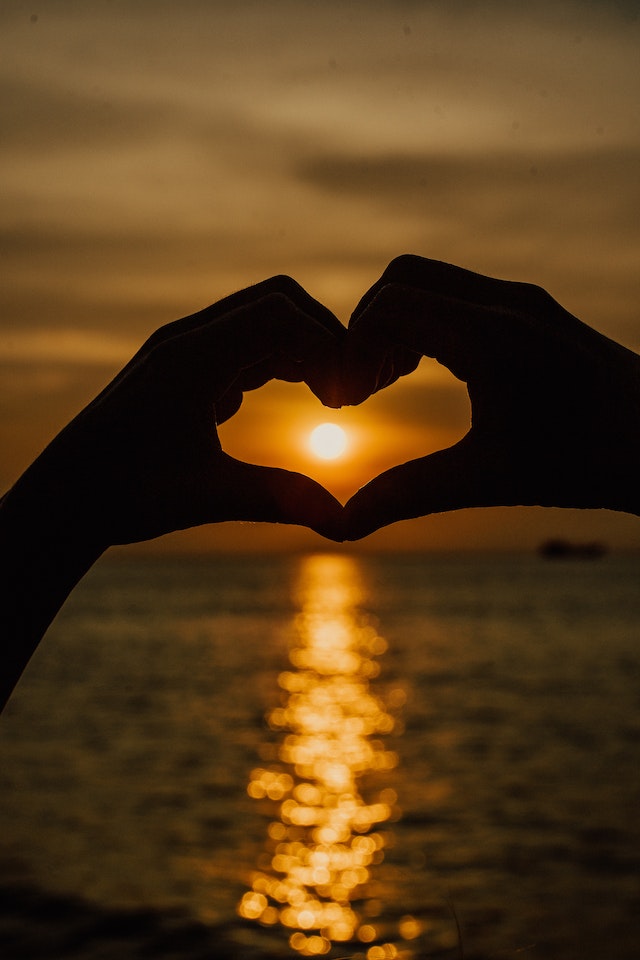 Silhouet van twee handen die een hart vormen met een zonsondergang op de achtergrond.