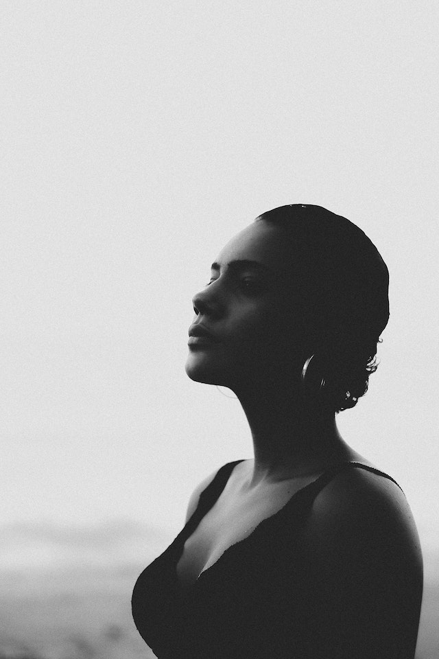 Woman looking to the left while on a beach in a grayscale photo.