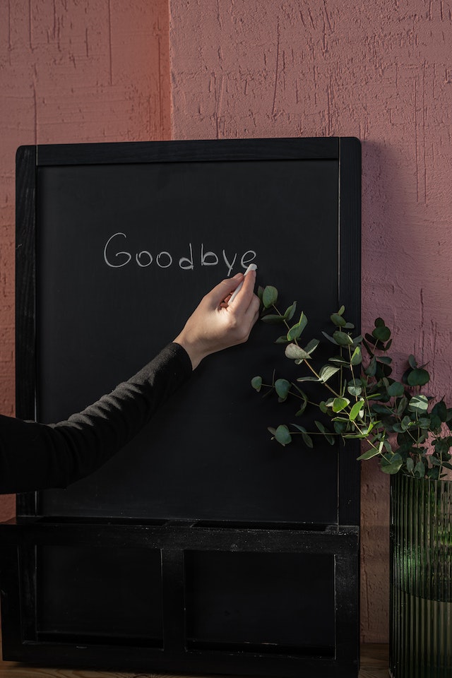 Person writing "GOODBYE" on black board with chalk