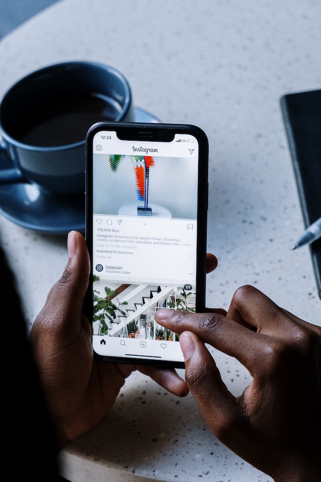 Pessoa invisível a segurar um iPhone preto enquanto faz scroll em Instagram.