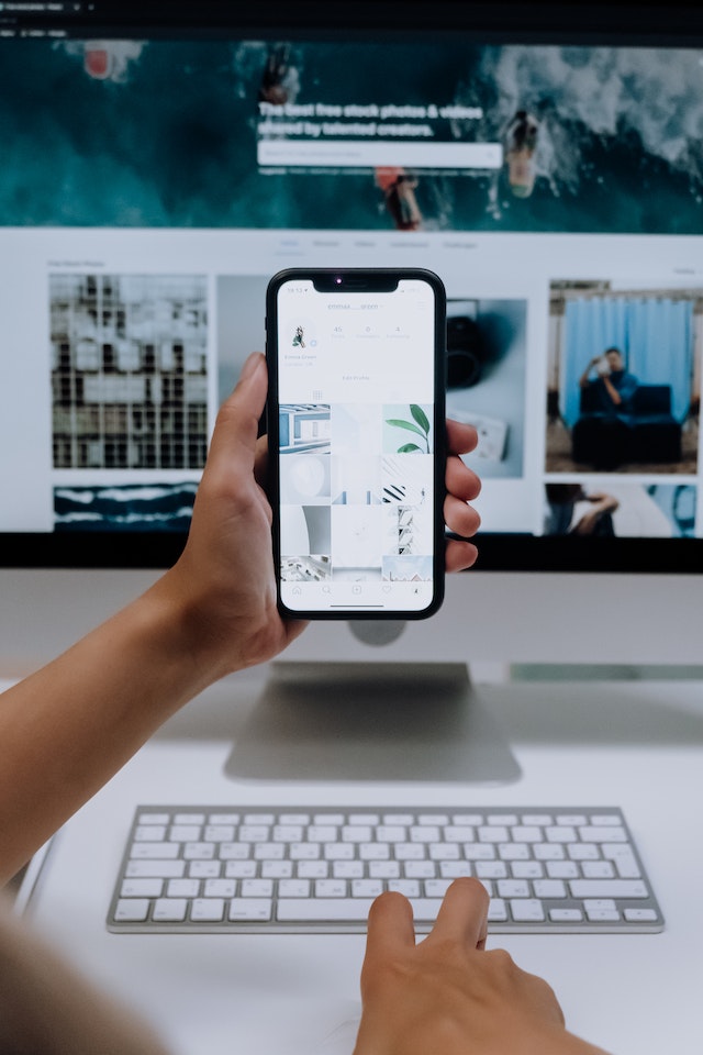 pexels-cottonbro-studio-5082576 | Path Social Hand in front of a computer holding white iphone displaying Instagram page with link in bio.