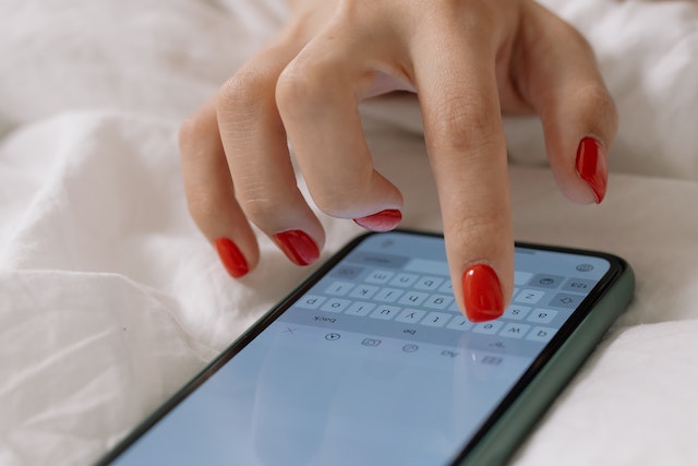 Hand of a person with manicured nails tapping on a smartphone screen.