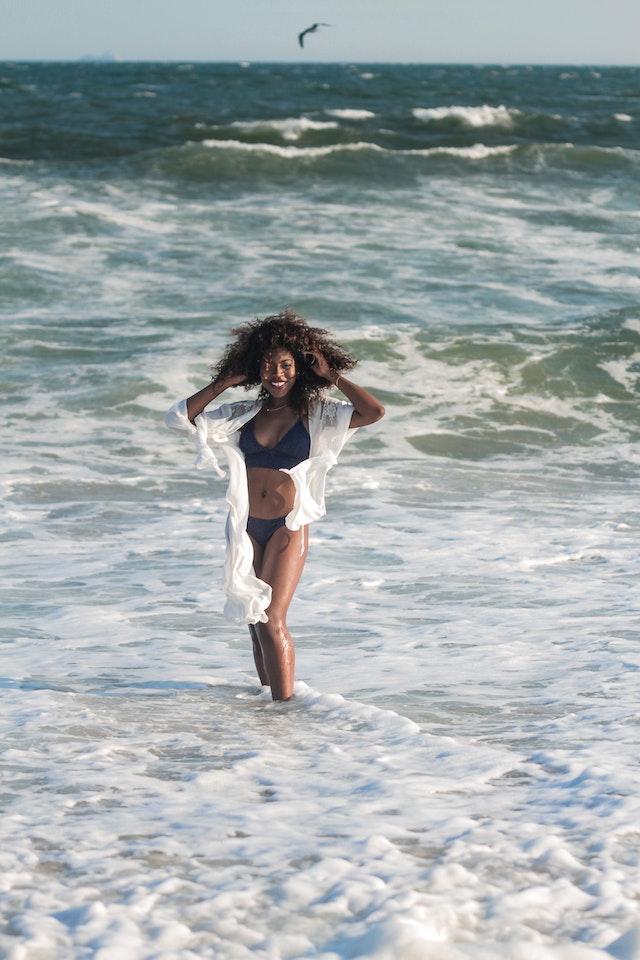 Photo of a smiling woman in a bikini posing by the beach.