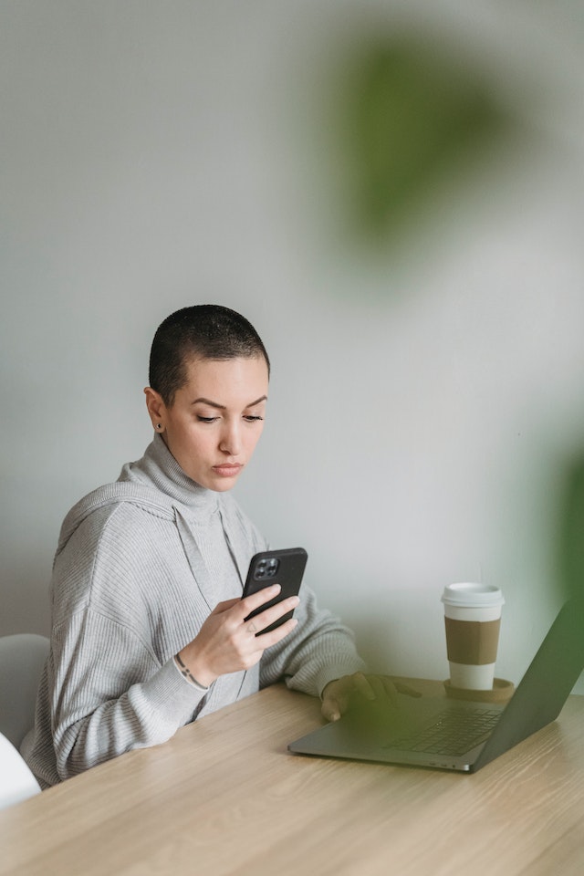 Geconcentreerde vrouw gebruikt smartphone en werkt op laptop.