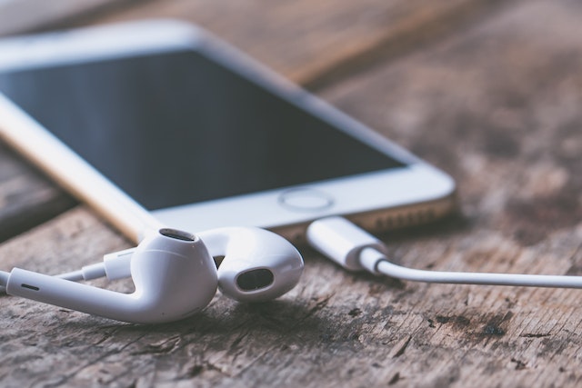 iPhone 7 dourado e auriculares lightning numa mesa de madeira.