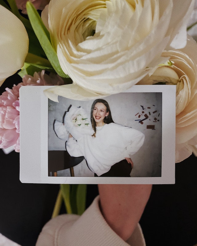 Una foto polaroid di una donna accanto a un bouquet. 