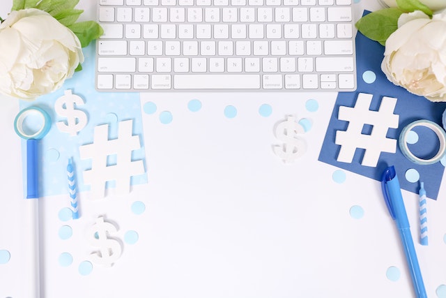 Tastatura de calculator alb lângă flori albe și hârtie colorată cu simboluri hashtag decupate.