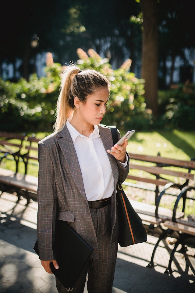 Une femme vérifie l'application Instagram Unfollow sur son téléphone dans un parc ensoleillé.