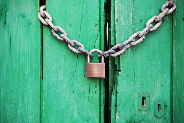 Cadeado de metal em latão com corrente em portas de madeira verde.