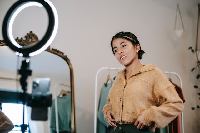 Woman smiling while recording a video with a ring light while trying on clothing.