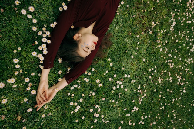 Woman in a maroon long-sleeve shirt lying in a field of white flowers.