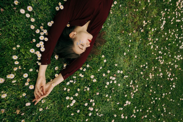 Femme vêtue d'une chemise à manches longues marron, allongée dans un champ de fleurs blanches.