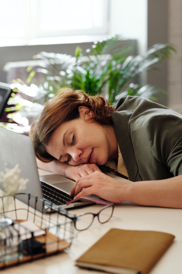 Woman laying her head down on her desk asleep next to her laptop.