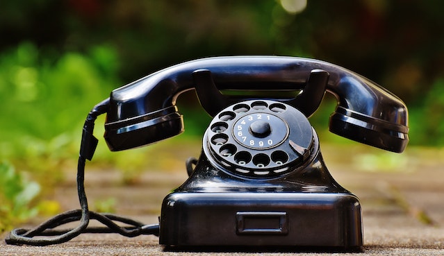 A black rotary phone sitting on a path.