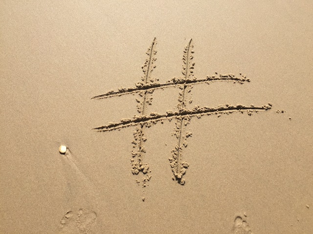 Sable de plage avec le symbole hashtag dessiné à côté d'empreintes de pas dans le sable.
