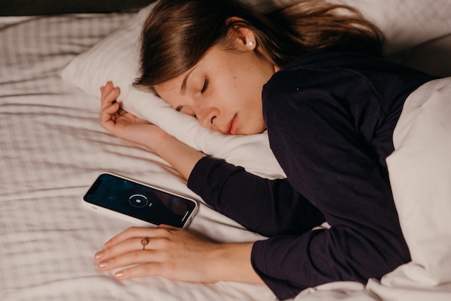 Woman asleep in bed with her cell phone beside her.