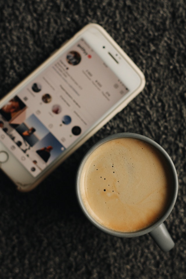 White iPhone with the Instagram app open beside a white ceramic mug with coffee.