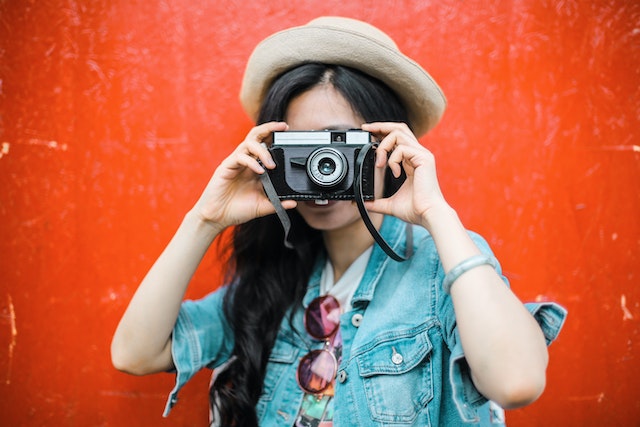 Vrouw houdt een zwarte camera omhoog om een foto te maken.