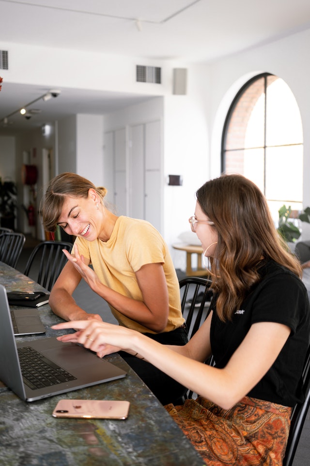 Foto van twee vrouwen die een gesprek voeren over iets dat ze op een computerscherm zien.