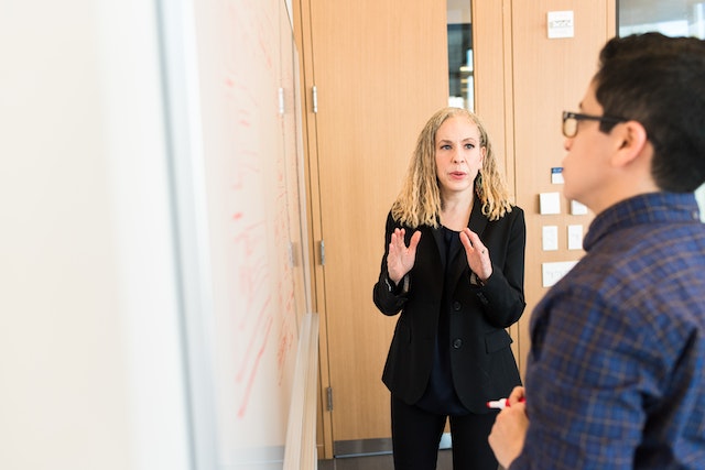 Vrouw in zwart pak staat bij het whiteboard