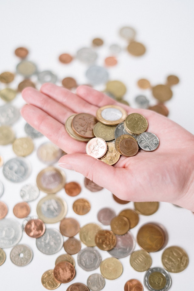 Hand einer Person, die Silber- und Goldmünzen über mehr verstreuten Münzen hält.