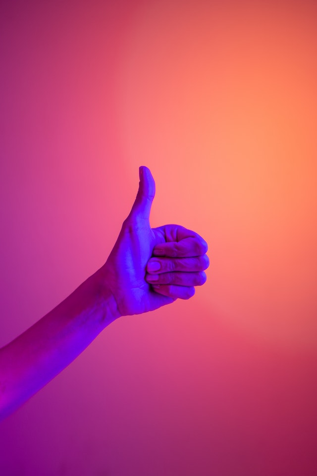 La mano de una persona levantando el pulgar iluminada con luces moradas y naranjas.